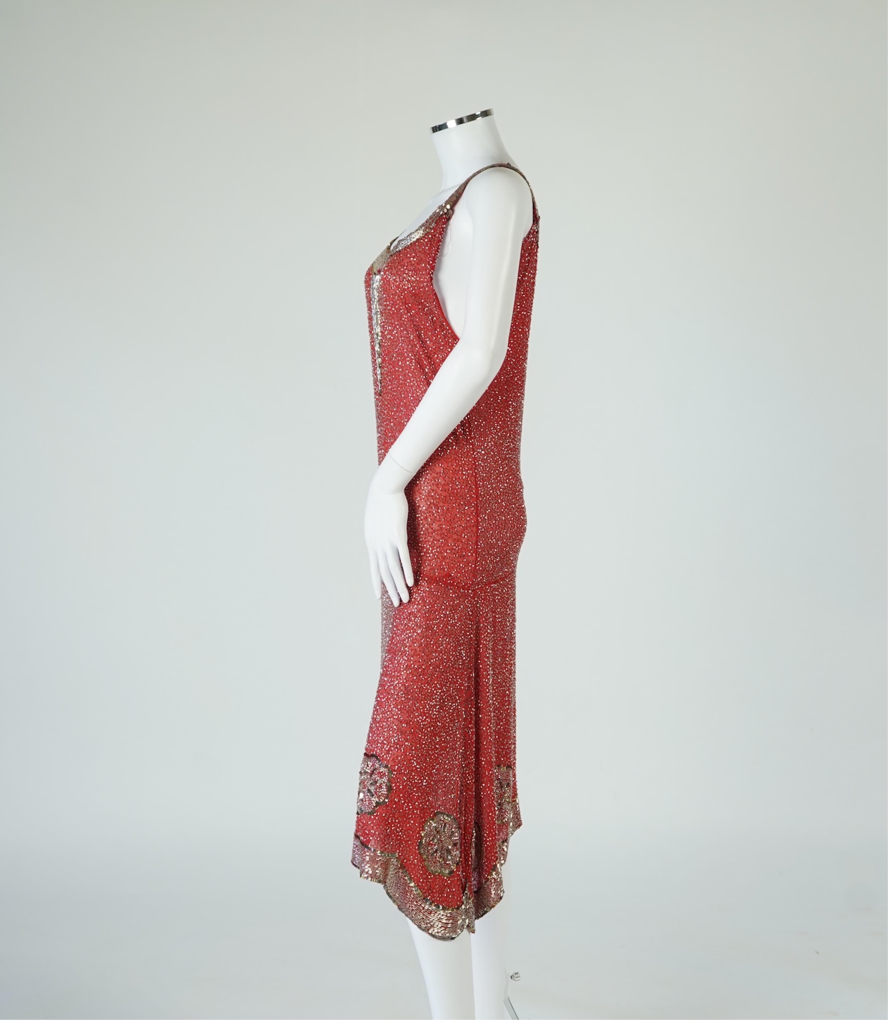 A 1920's red georgette beaded evening dress. Hand beaded and sequinned in white and gold, designed with a dropped waist, handkerchief points and wide beaded border with large stylistic floral motifs. Length 115cm. Condit